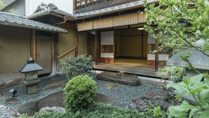 Ein traditionelles japanisches Gebäude mit Holzfassade, einem Steintorii und einem Garten mit Steinen und Pflanzen.