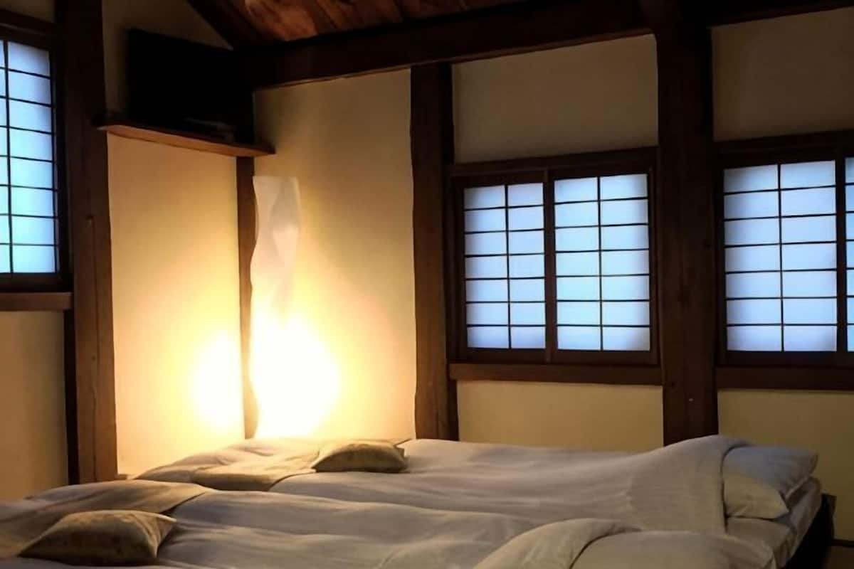 A traditional Japanese-style room with tatami flooring, a low wooden bed, and shoji screens.