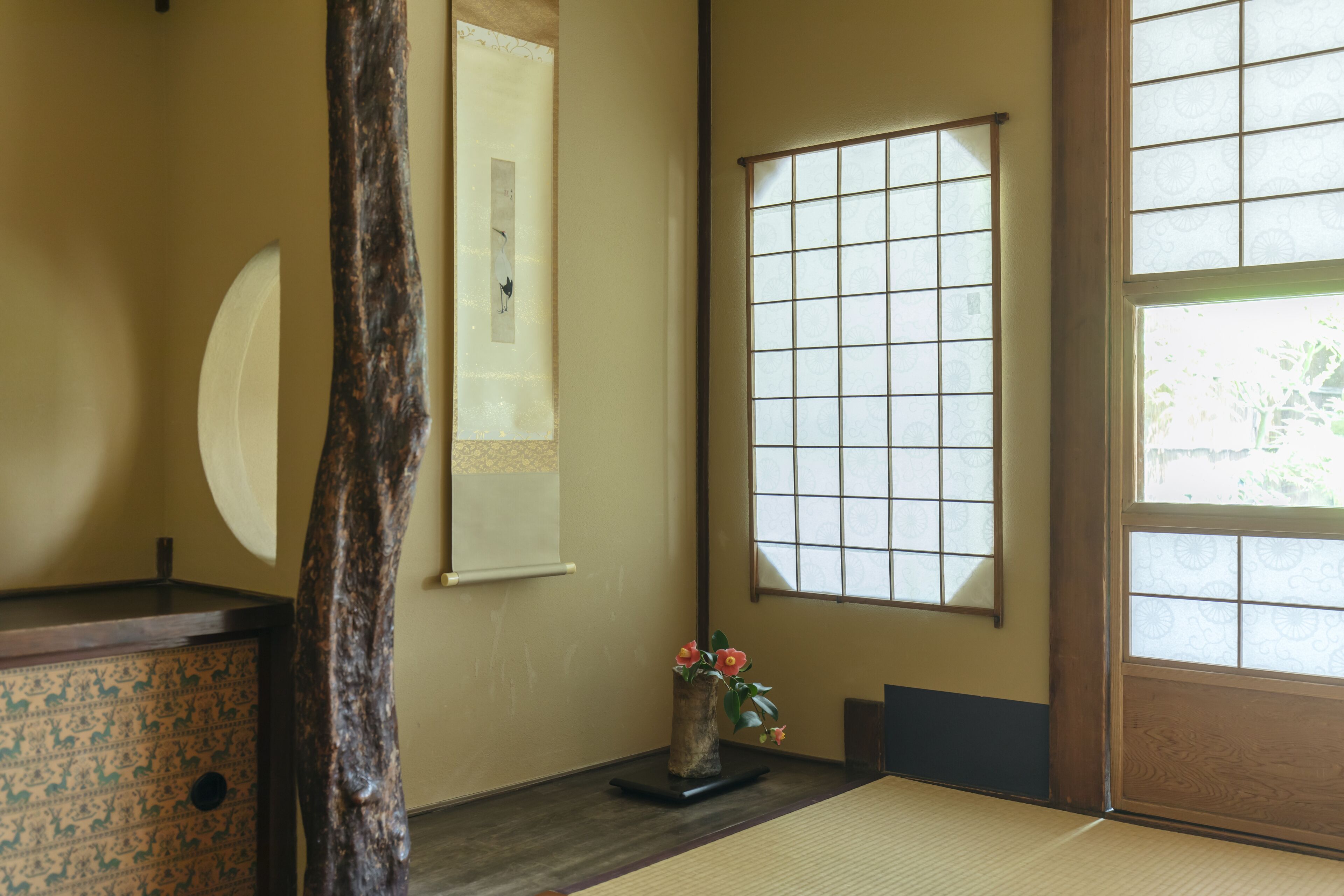 A traditional Japanese room with tatami flooring, a shoji screen, and a wooden desk with a vase of flowers.