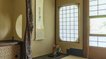 A traditional Japanese room with tatami flooring, a shoji screen, and a wooden desk with a vase of flowers.