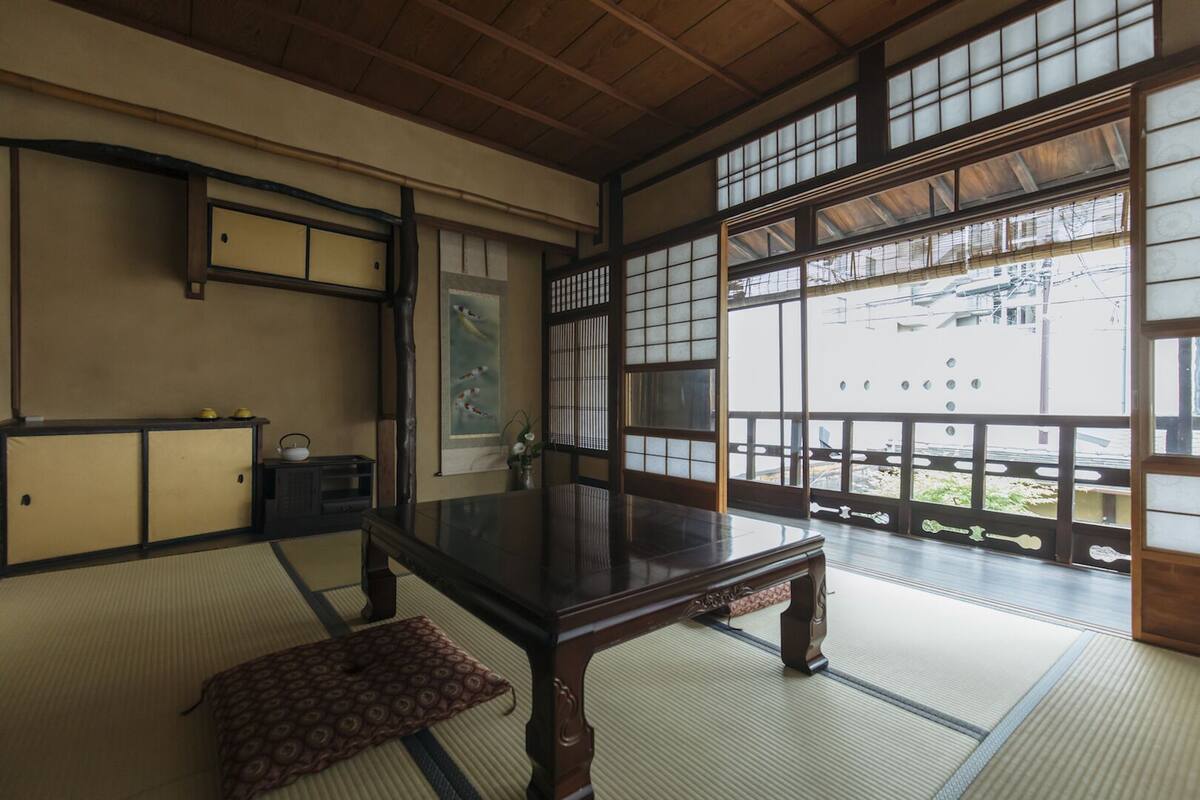 Une pièce de style japonais traditionnel, avec un sol recouvert de tatamis, une petite table en bois, des portes coulissantes et une vue sur l’extérieur.