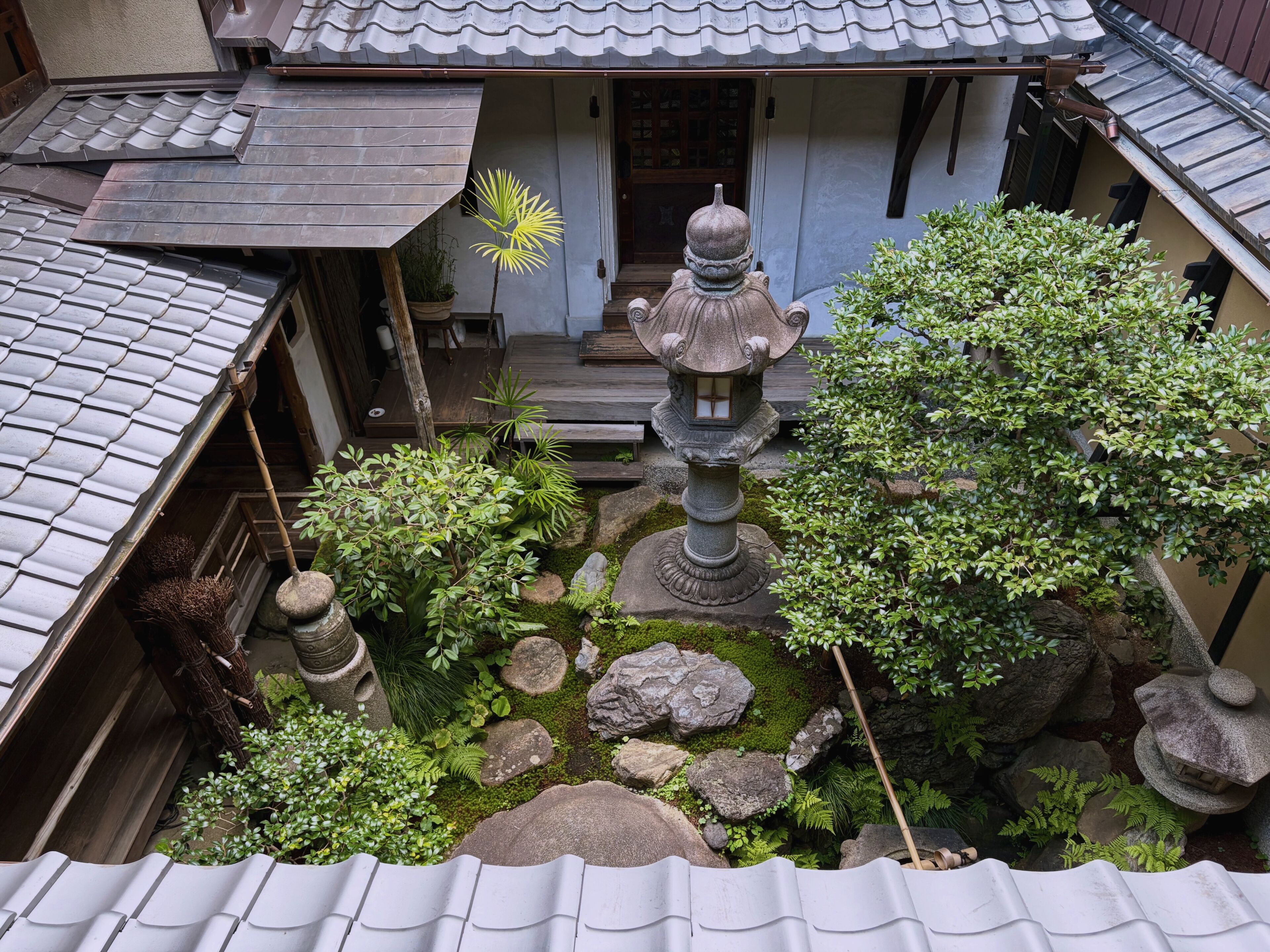 A traditional Japanese garden with a stone lantern, rock formations, and a wooden building with a tiled roof.