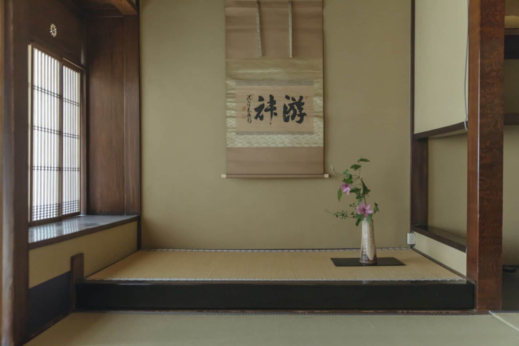 A traditional Japanese room with tatami flooring, a shoji screen, and a calligraphy scroll.