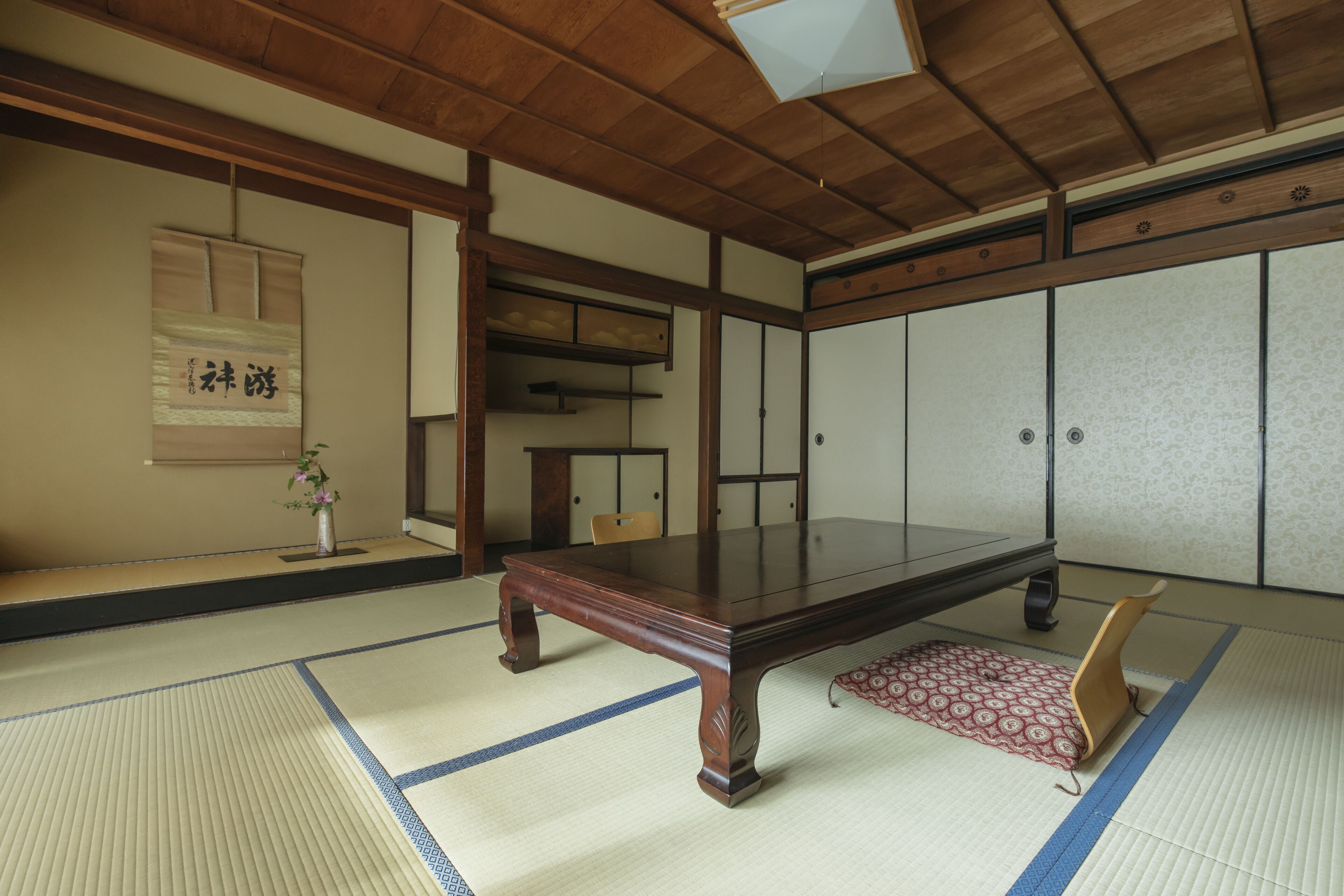 Una habitación con suelo de tatami, una mesa de madera, un taburete bajo y puertas correderas tradicionales.