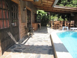 A stone patio with a pool, wooden furniture, and a brick wall. - XPAI Guesthouse (Pai)