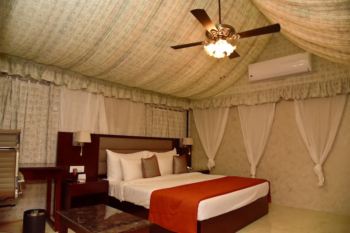 A hotel room with a large bed, a ceiling fan, an air conditioner, and curtains.