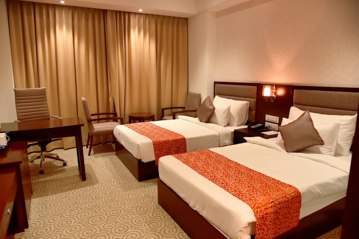 A hotel room with two beds, a desk, and a chair.