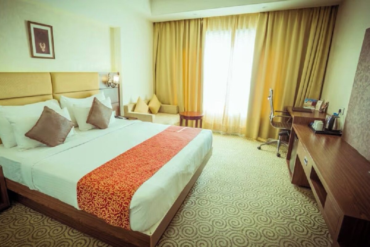 A hotel room with a bed, a desk, a chair, a lamp, and a television.