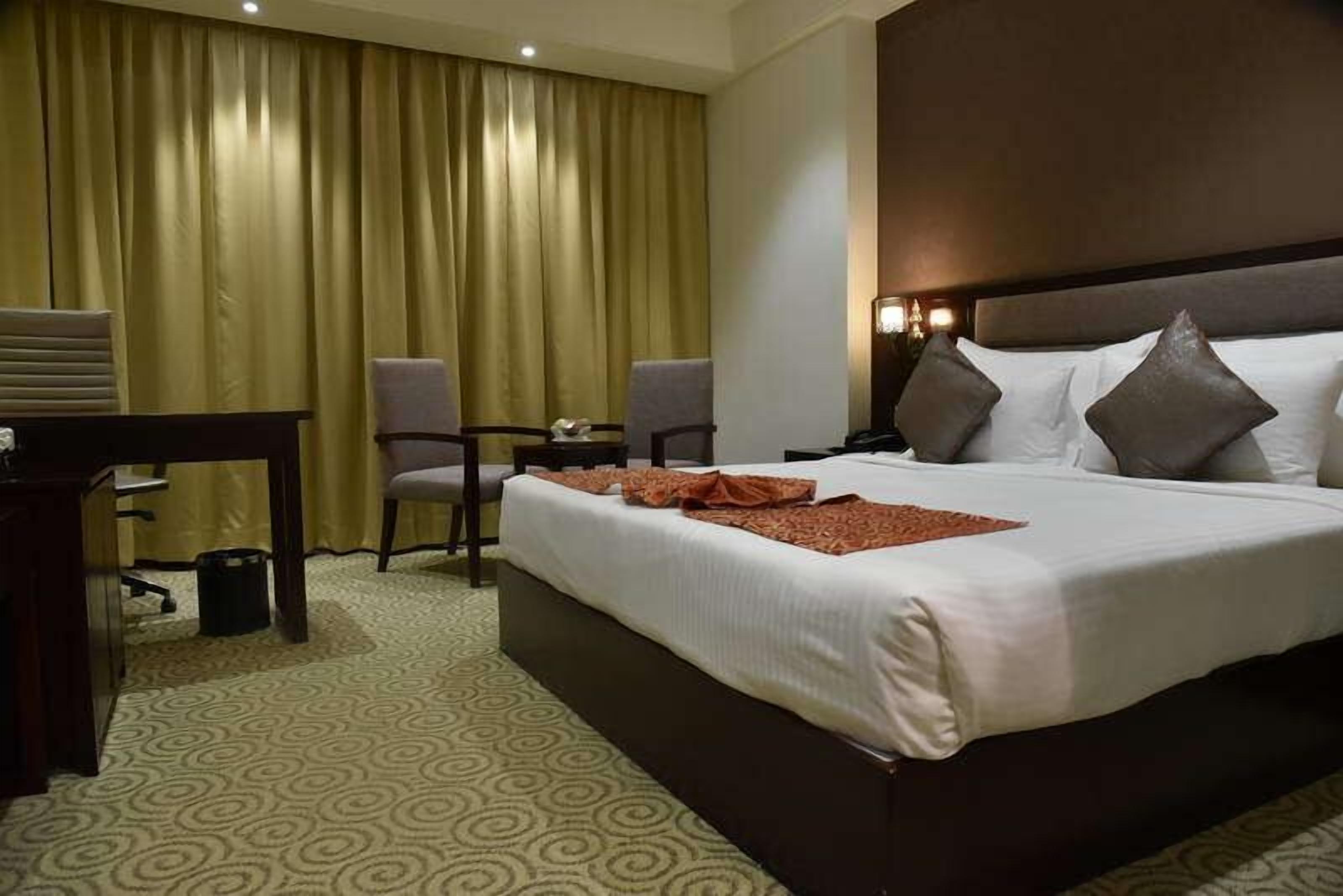 A hotel room with a large bed, two chairs, a desk, and a curtain.