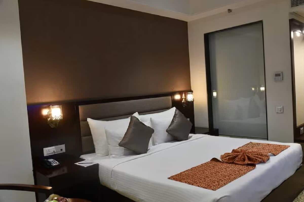 A hotel room with a large bed, a nightstand with a phone, and a wall-mounted light fixture.