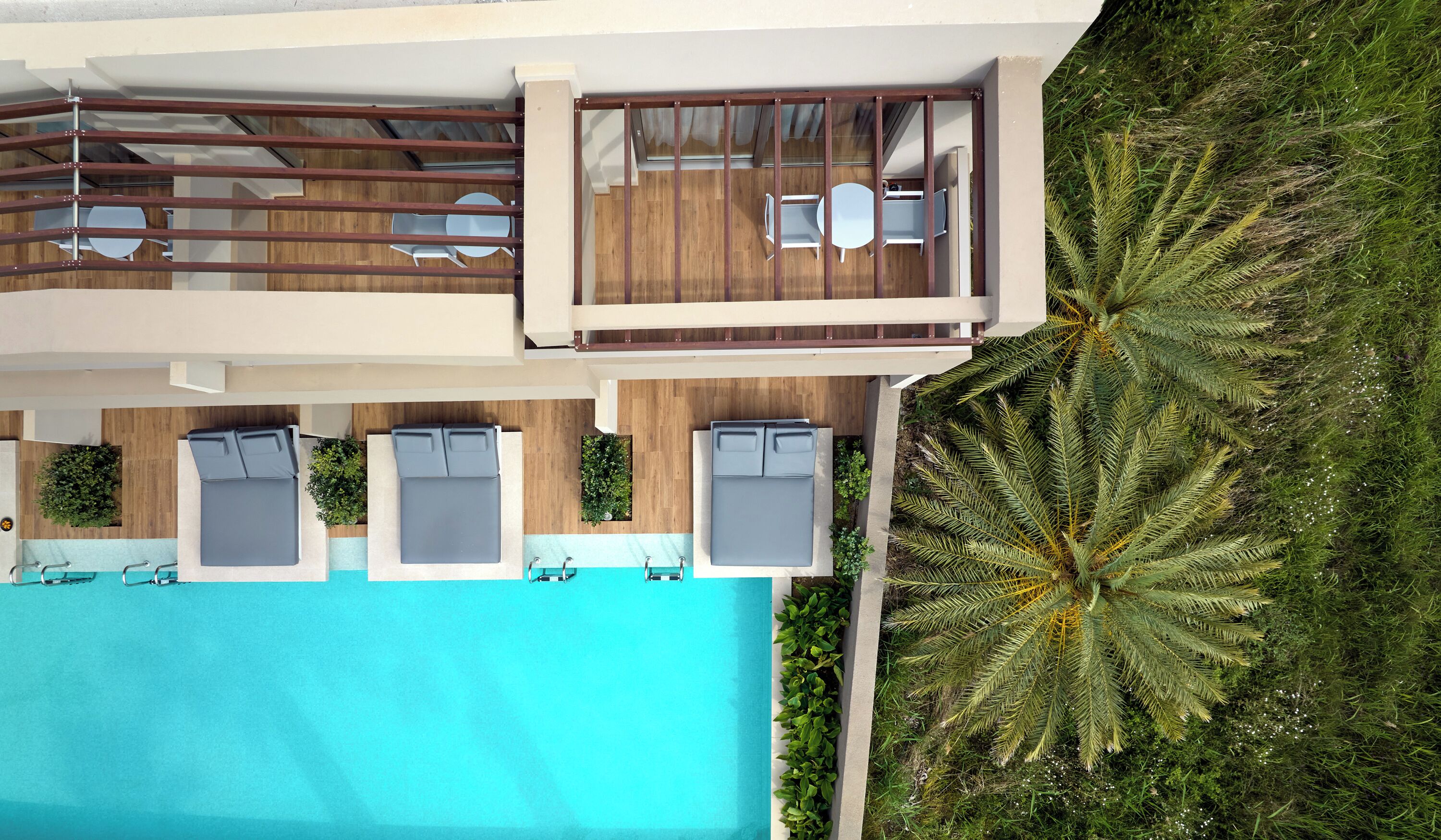 An aerial view of a modern hotel with a rooftop pool, lounge chairs, and a lush green landscape.