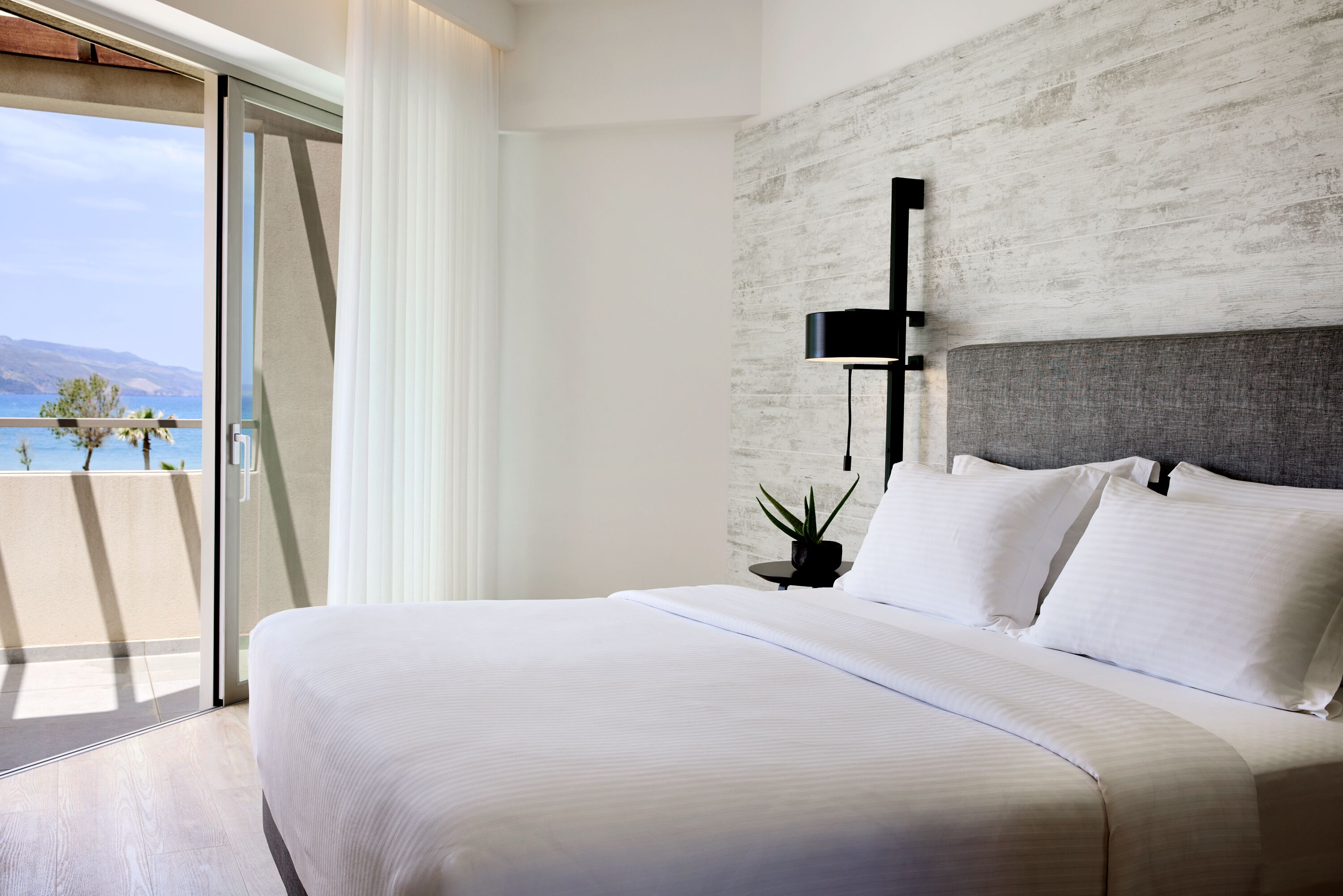 A modern bedroom with a large bed, a view of the sea, and a minimalist design.