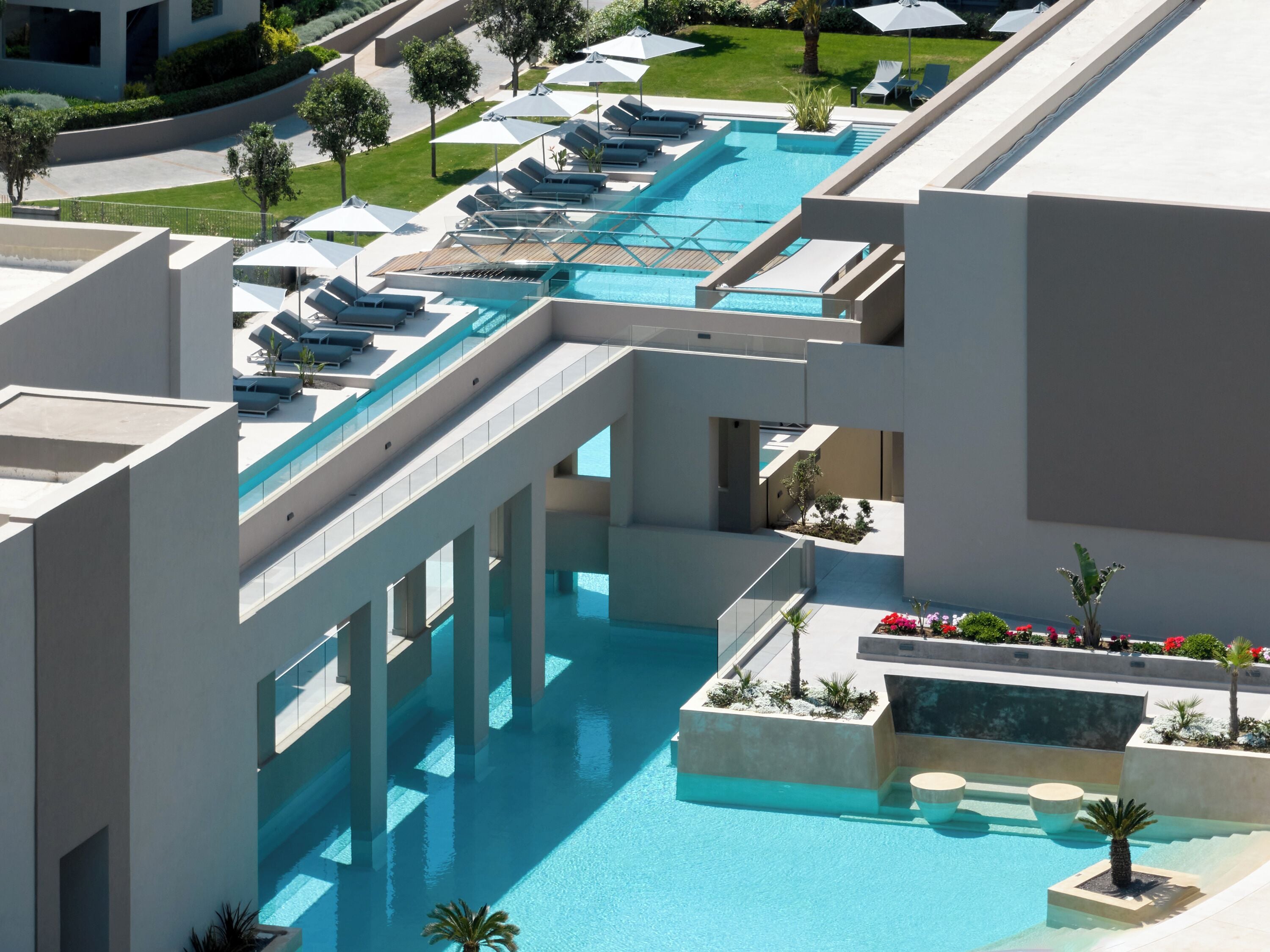 Un hotel moderno con una amplia piscina central, varias zonas de descanso y un jardín bien cuidado.