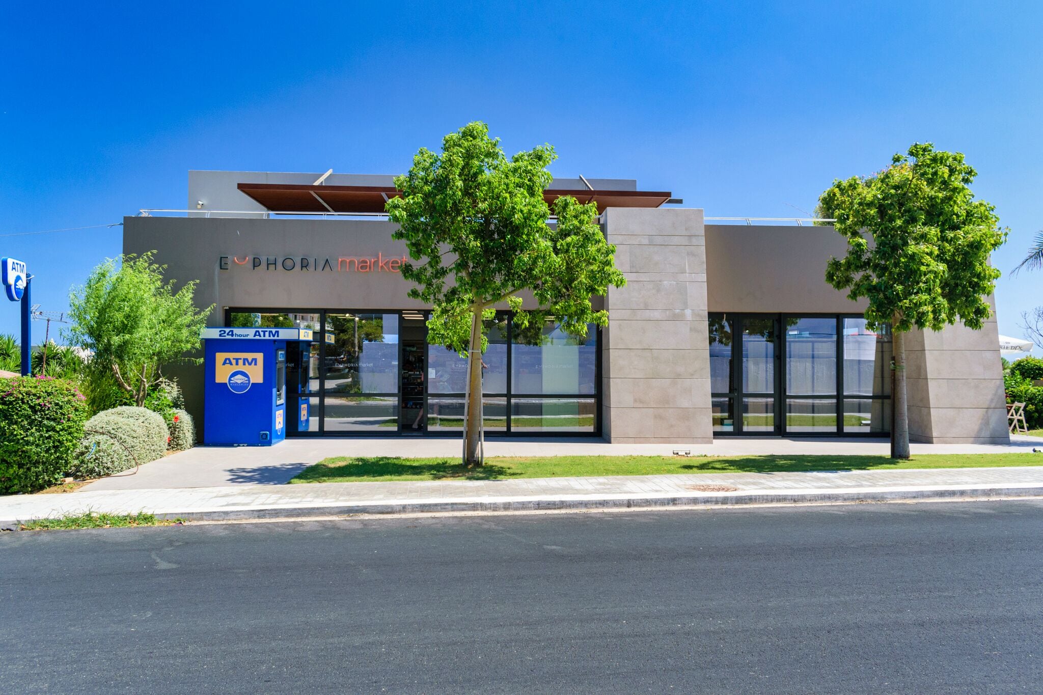 A modern building with a 24-hour ATM, glass doors, and a landscaped area with trees.