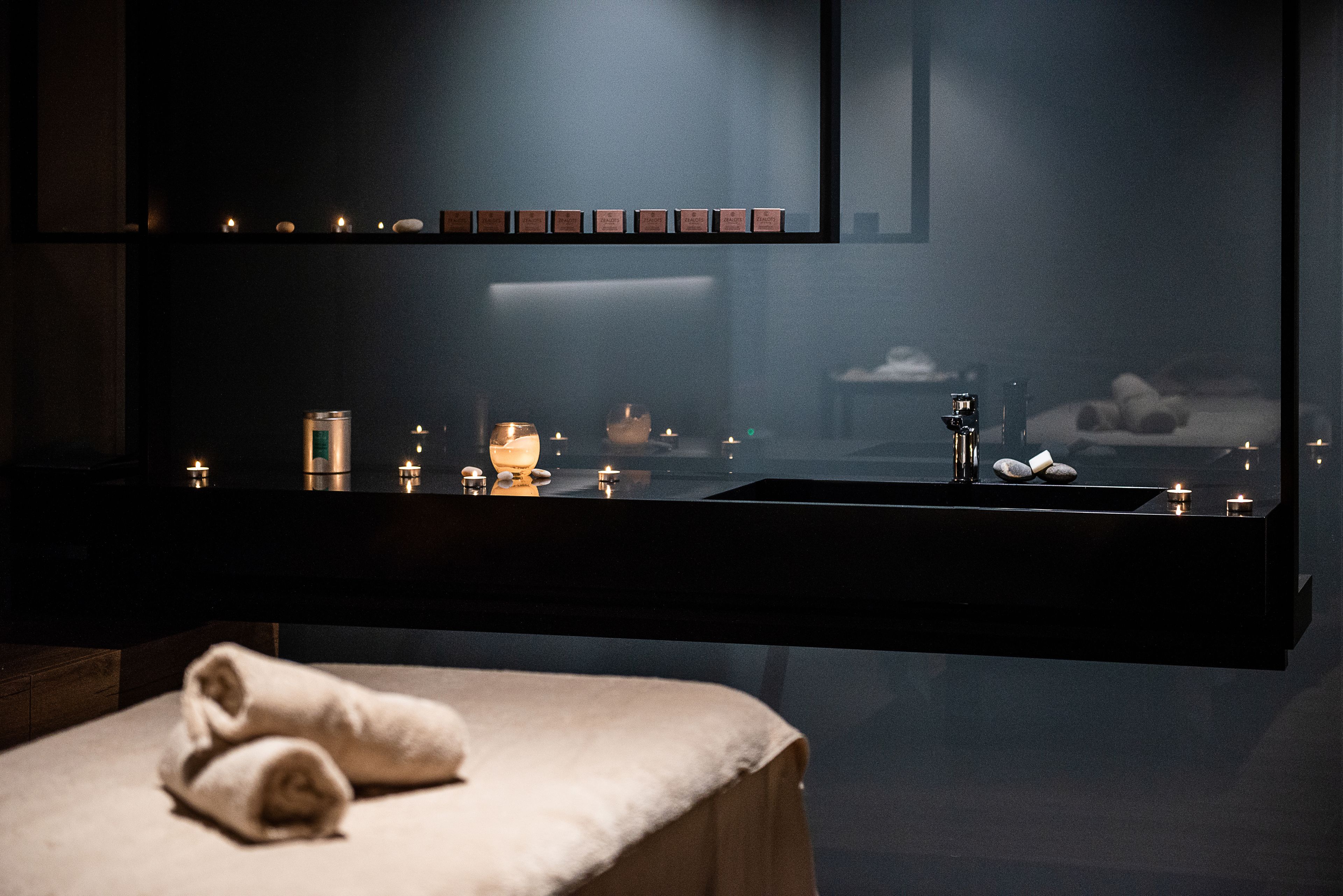 A dimly lit spa area with a large mirror, candles, and a towel on a bench.