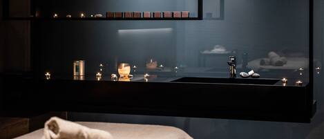 A dimly lit spa area with a large mirror, candles, and a towel on a bench.