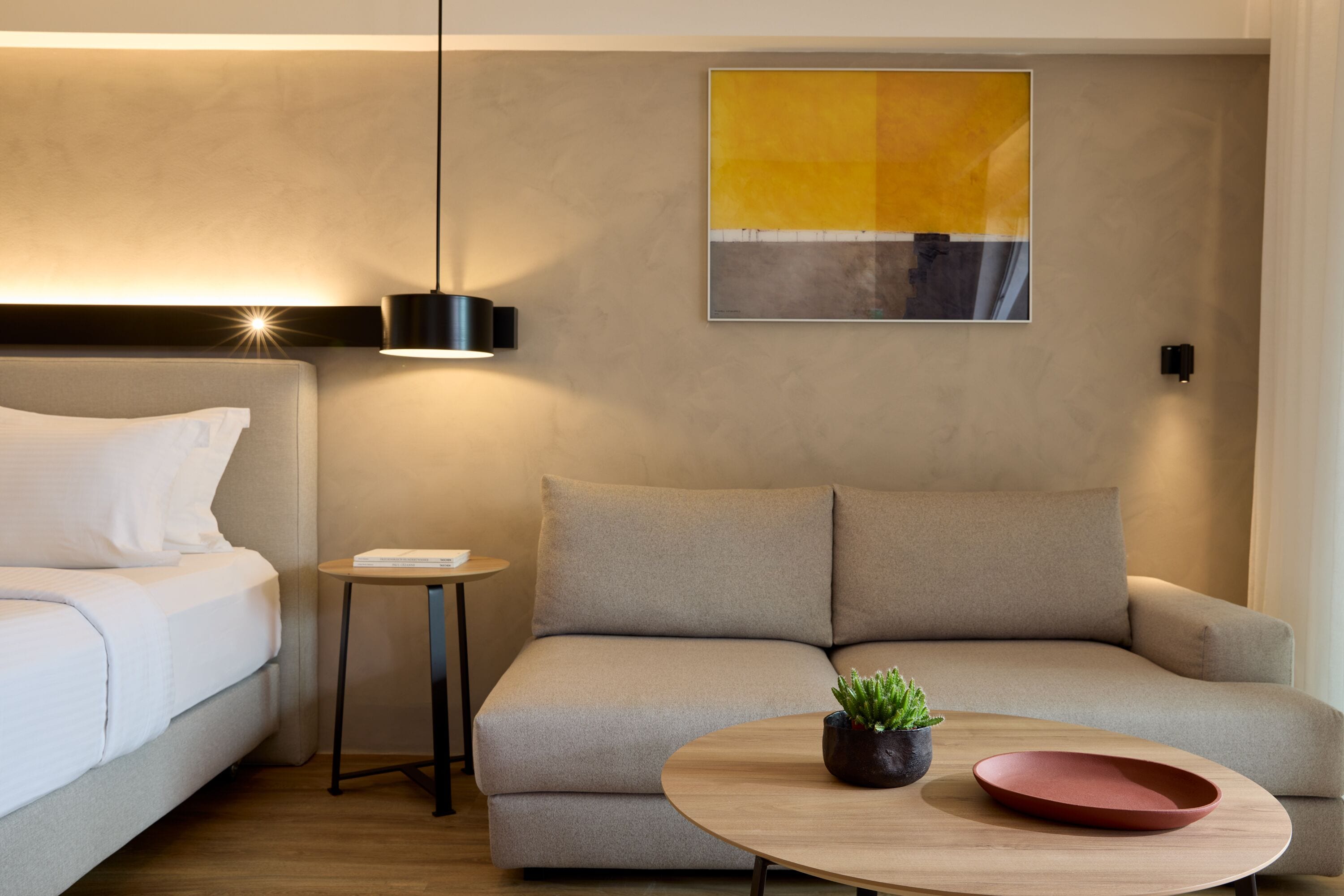 A modern hotel room with a sofa, a small table with a plant, and a wall-mounted artwork.