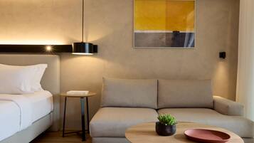 A modern hotel room with a sofa, a small table with a plant, and a wall-mounted artwork.