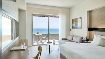 Habitación de hotel con una cama grande, zona de estar con una mesa y sillas, y balcón con vista al mar.