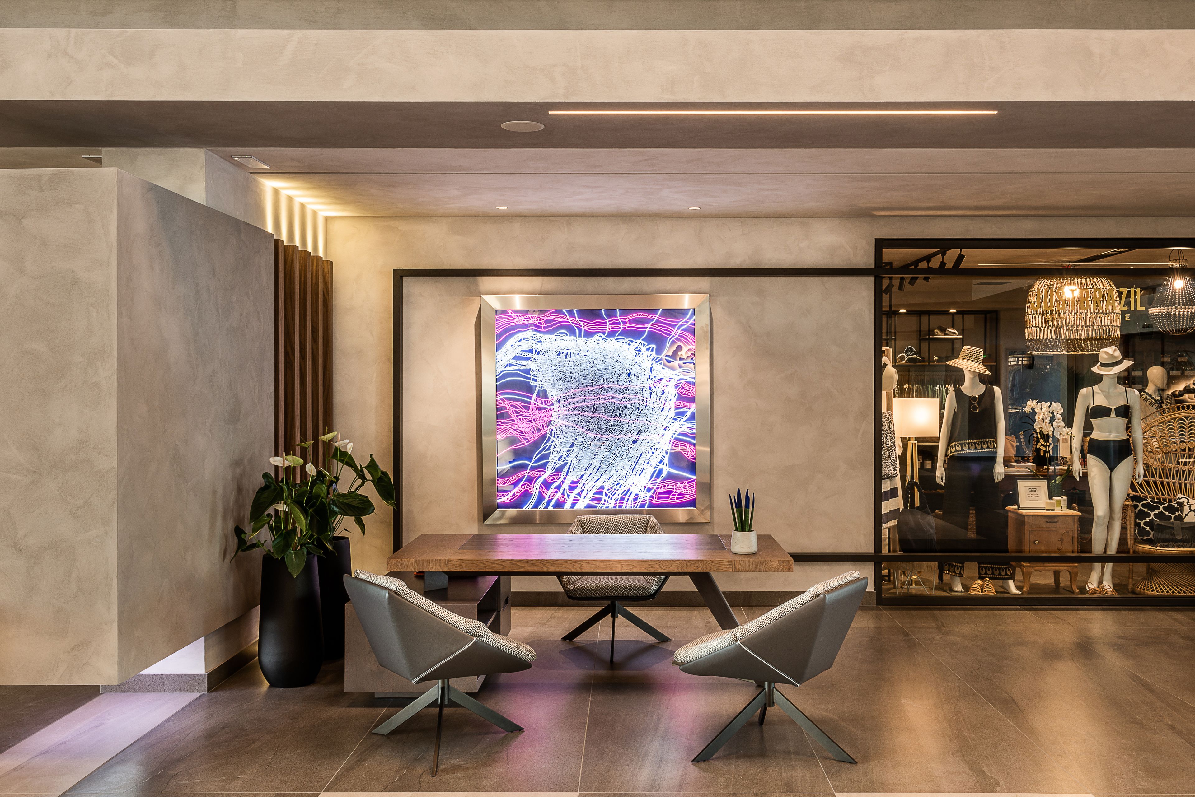 A modern interior with a wooden table and two chairs, a large abstract artwork, and a store window with mannequins.
