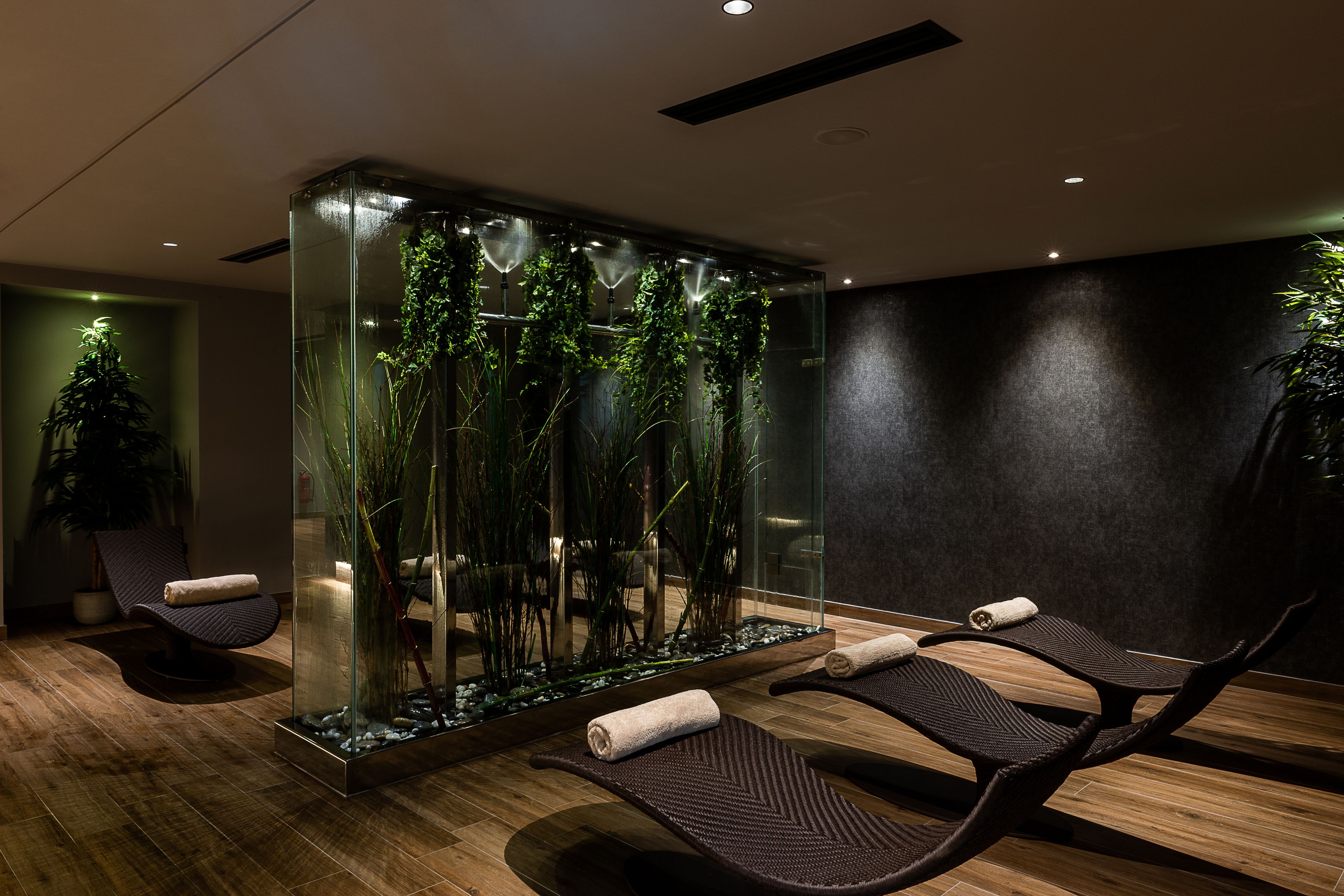 Un spa moderno con mampara de vidrio, suelo de madera y dos sillones reclinables con toallas.