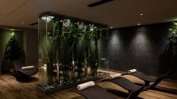 Un spa moderno con mampara de vidrio, suelo de madera y dos sillones reclinables con toallas.