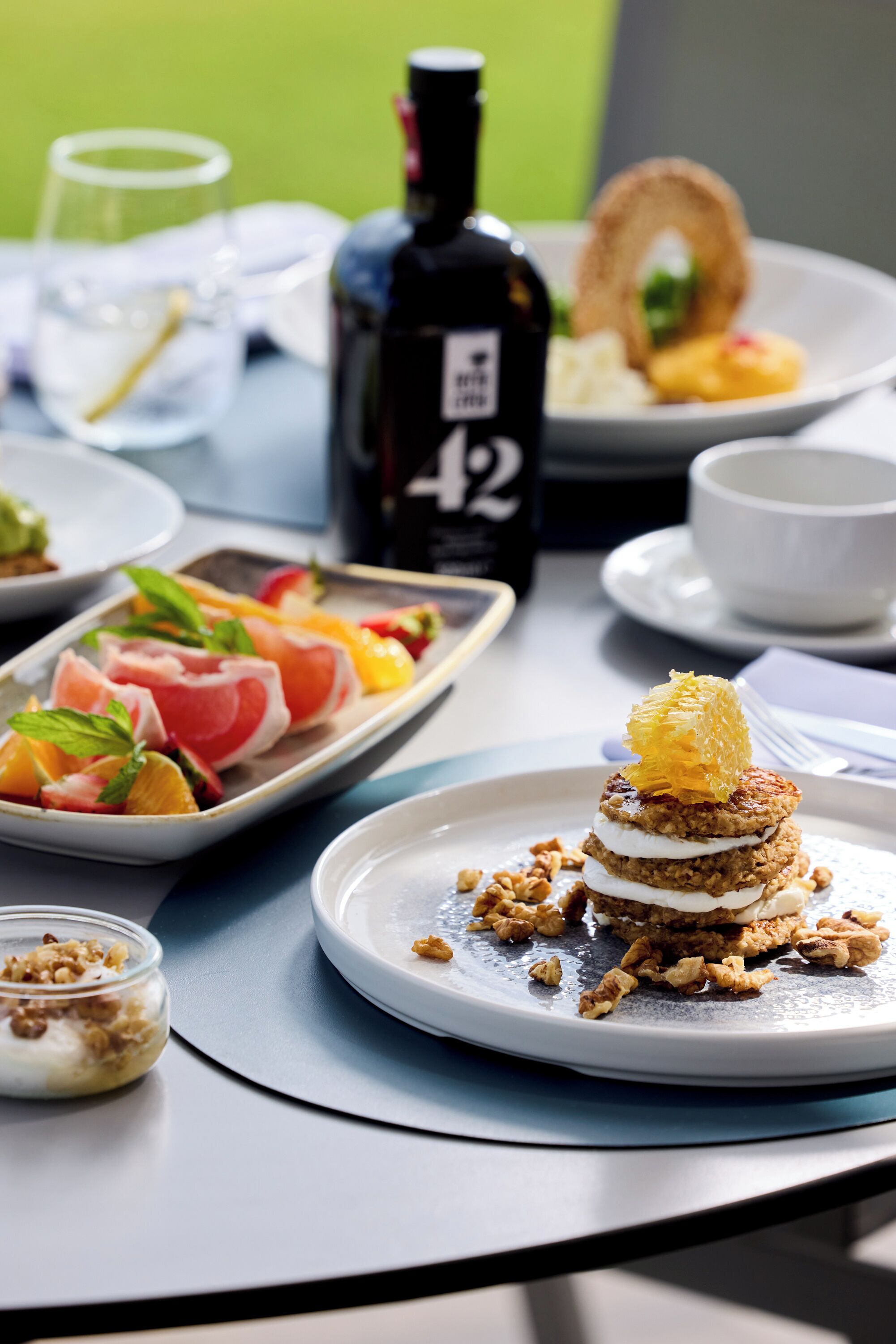 A table with various dishes, including a plate with a layered dessert, a bowl of granola, and a plate of fruit salad.