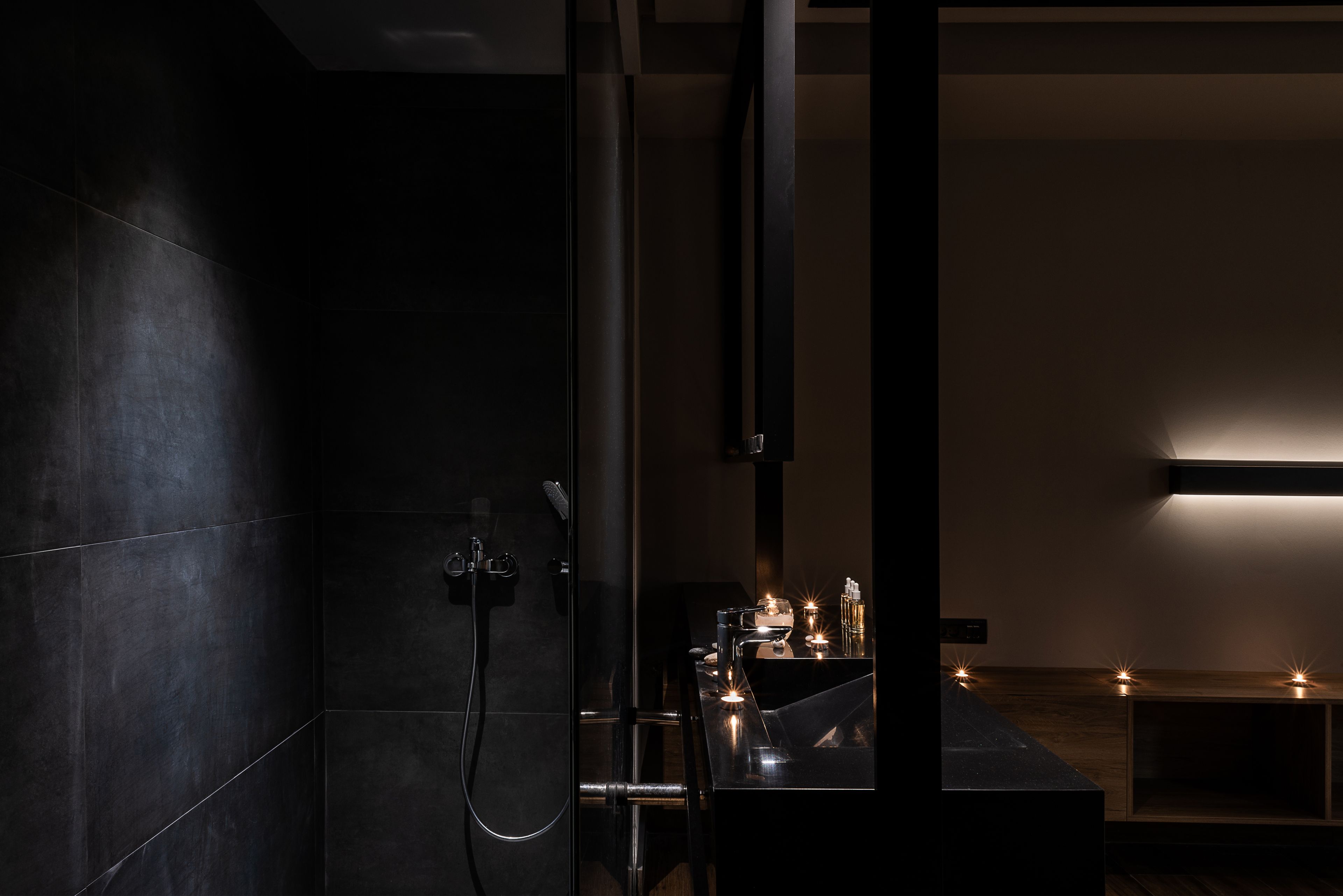 Uma casa de banho moderna com azulejos escuros, chuveiro e um lavatório com velas.