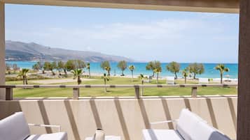 Un balcone con arredi da esterno bianchi, un vaso e vista su una spiaggia con palme e montagne sullo sfondo.