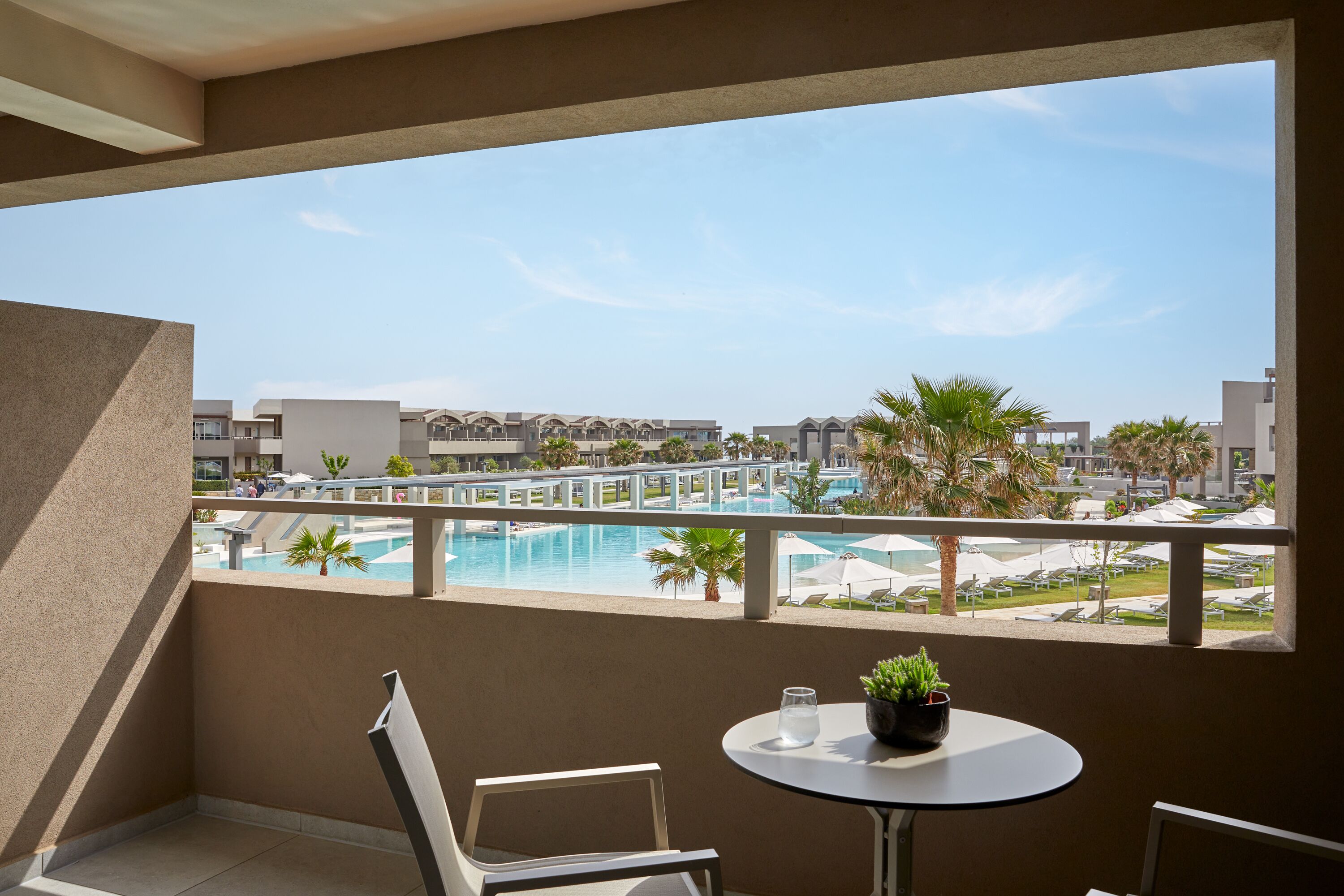 A balcony with a view of a swimming pool, palm trees, and hotel buildings.
