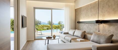 Una sala de estar moderna con un sofá, una mesa de centro y un televisor. Se ve una ventana grande con vista a una piscina y follaje.