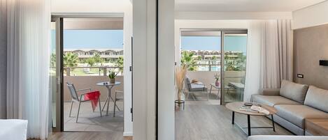 A modern hotel room with a balcony, a sofa, a coffee table, and a dining area with a table and chairs.