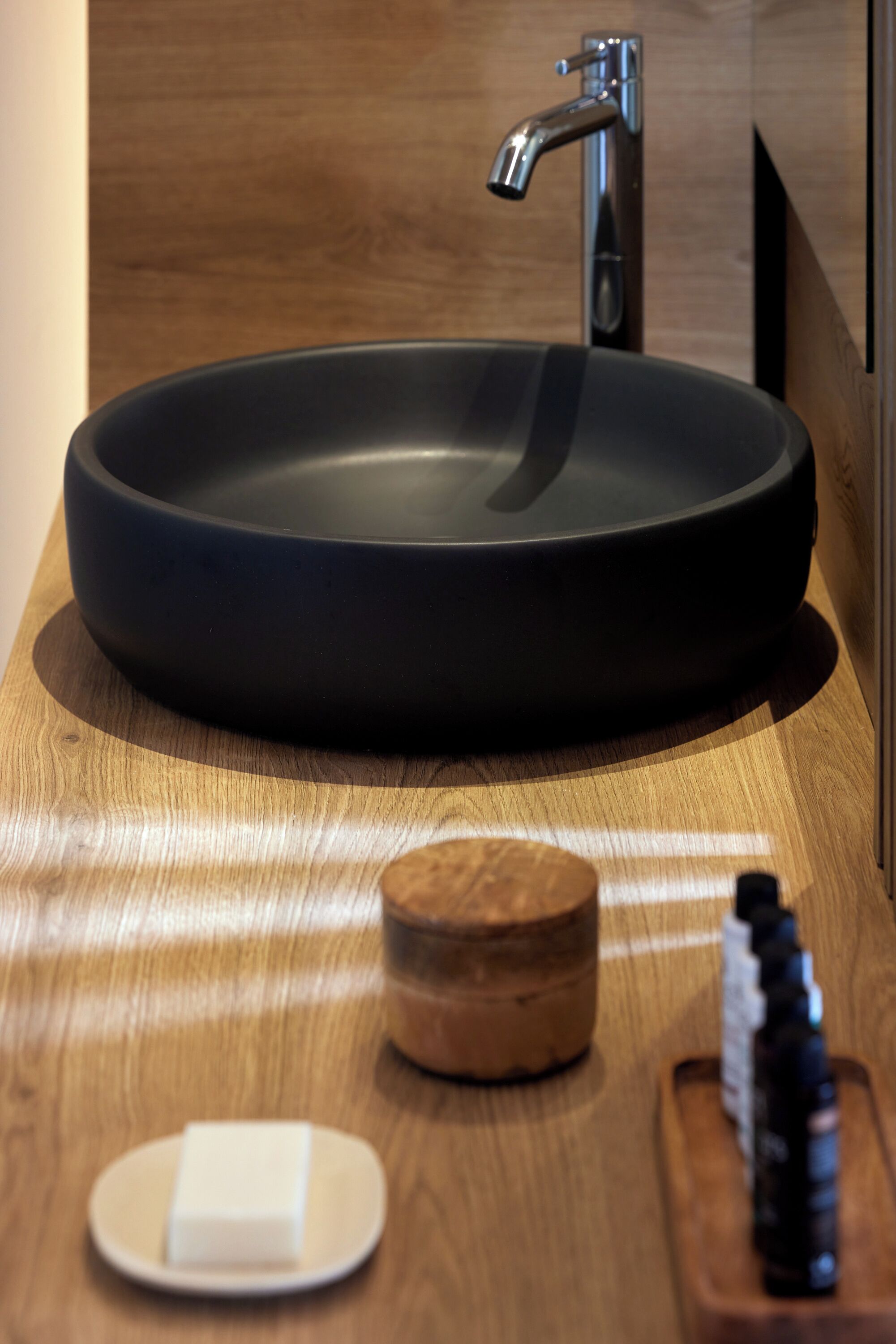 A modern bathroom with a round black sink, a wooden vanity, a soap dish, and a bottle of liquid soap.
