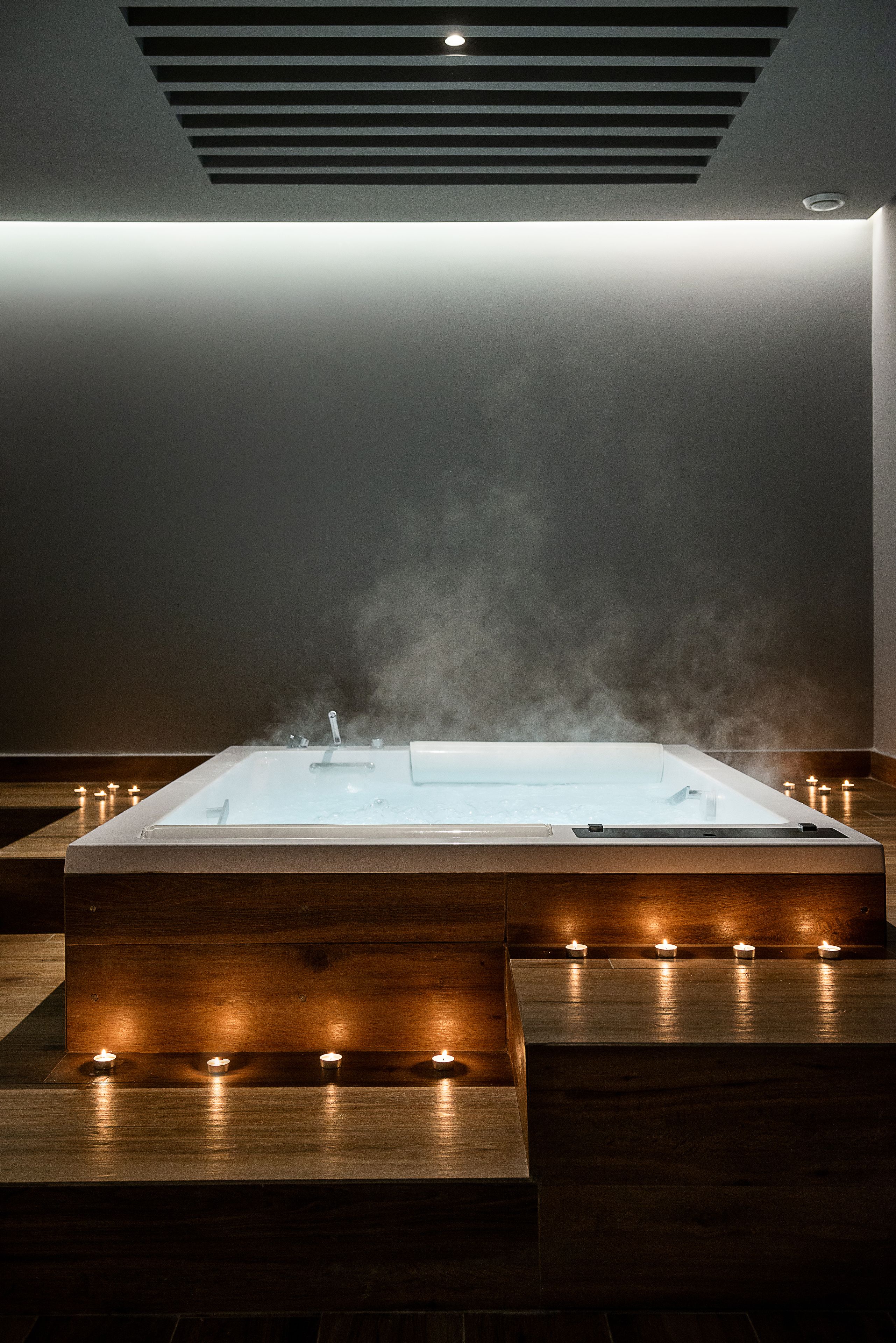A spa area with a hot tub, steam rising, and candles on wooden platforms.