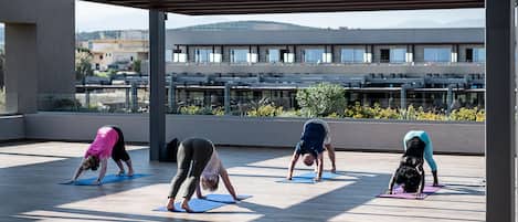 Four people doing yoga on blue mats under a covered area with a view of buildings and mountains in the background.