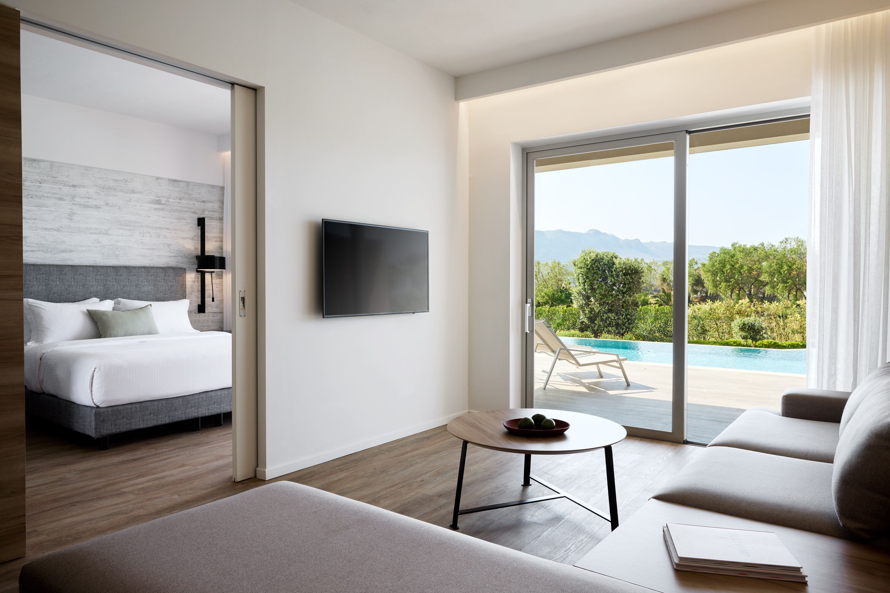 Habitación de hotel moderna con cama, sofá, una mesita, televisor y balcón con vista a la piscina.