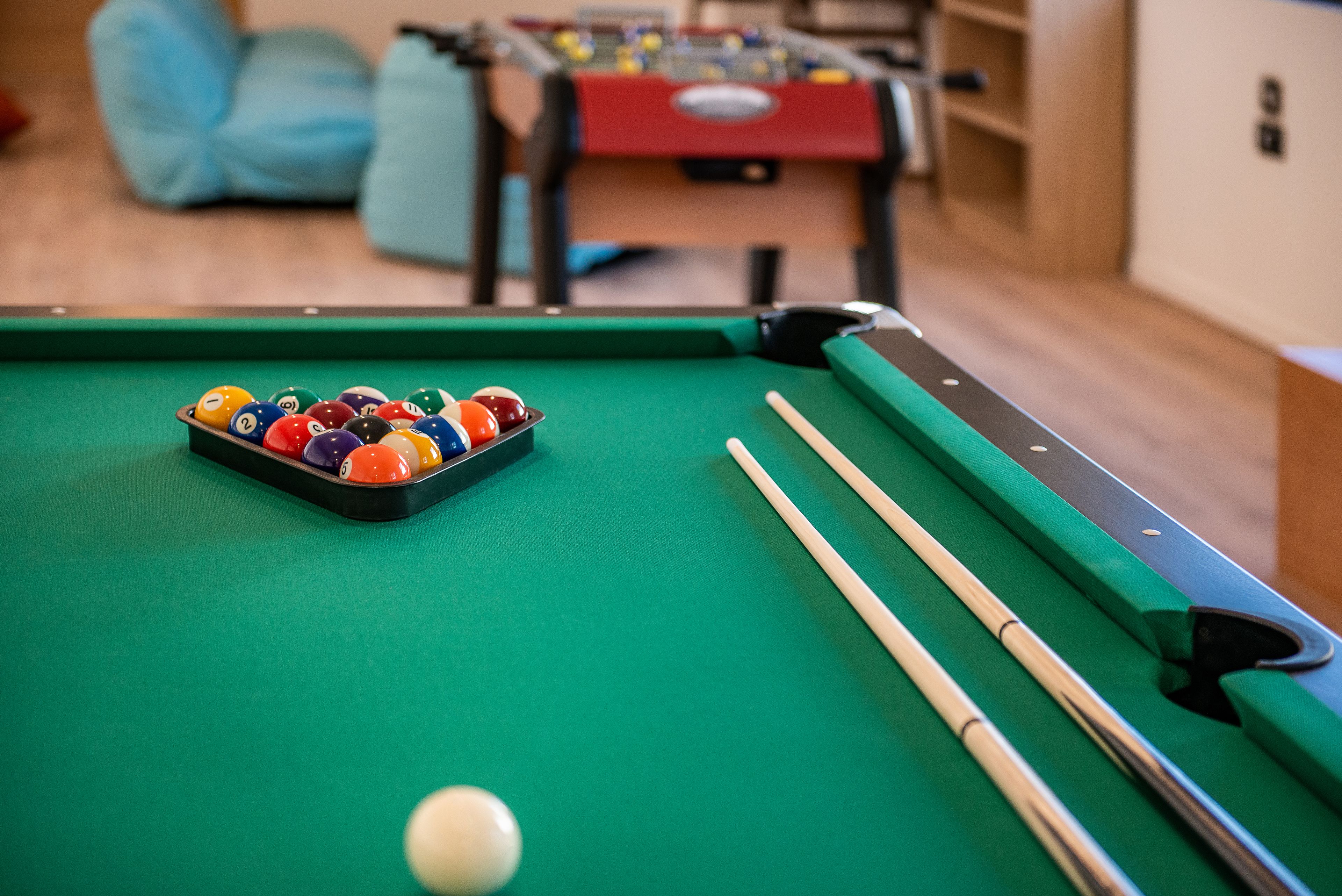 A pool table with balls and cues, a red table tennis table, and a sofa in the background.