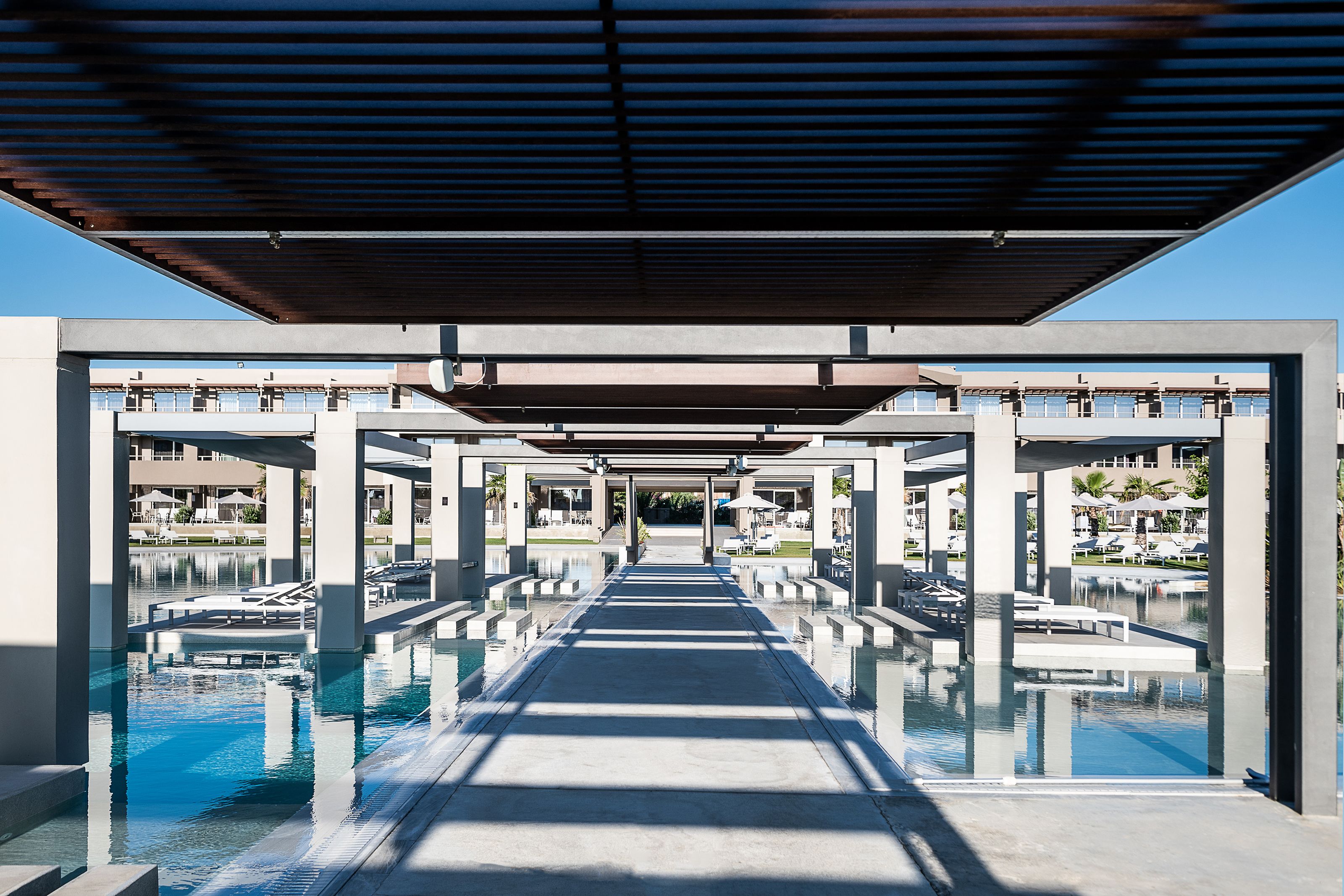A modern pool area with clear water, concrete pathways, and a covered walkway.