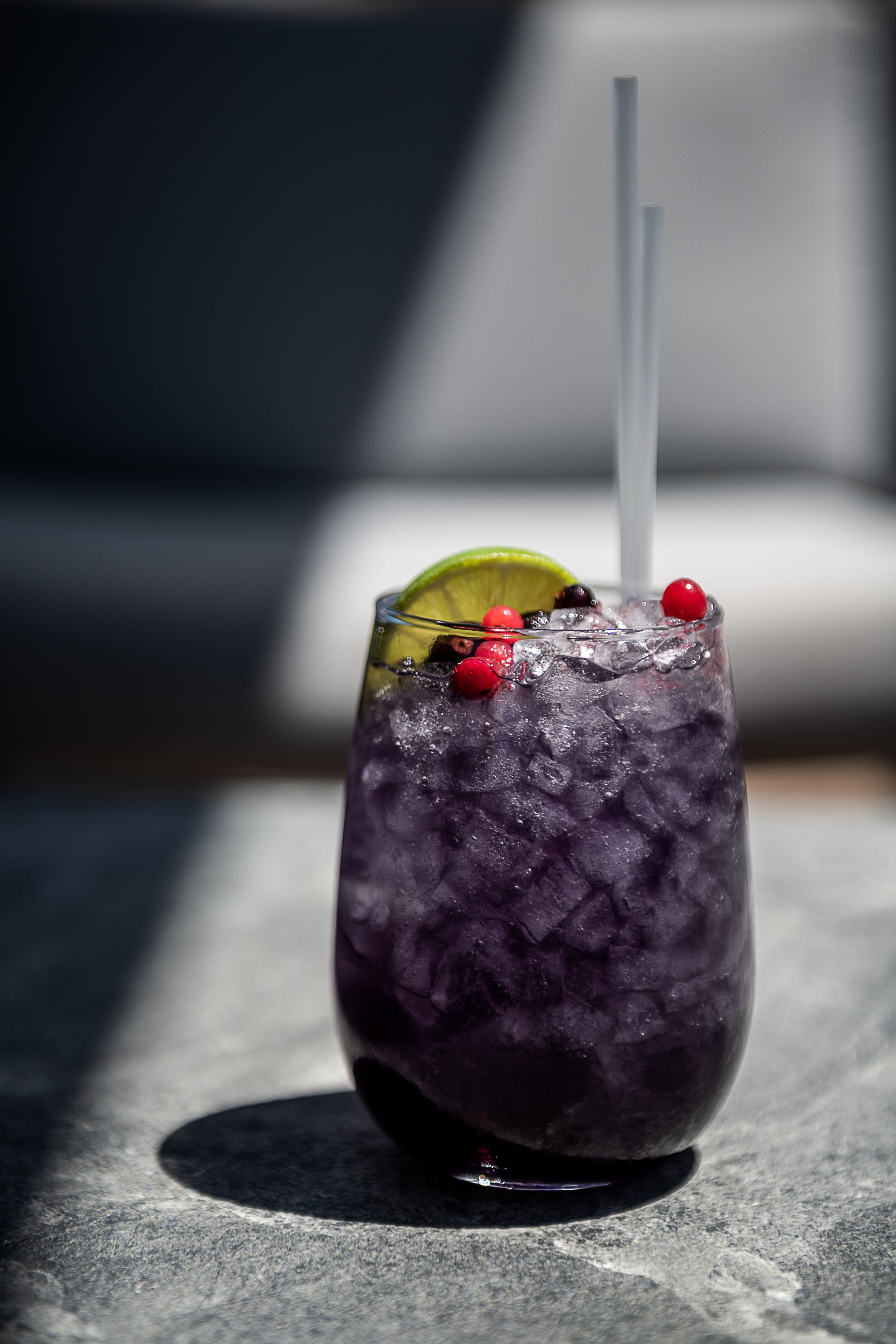 Un vaso de bebida morada con hielo, adornado con una rodaja de lima y bayas rojas, y una pajita.