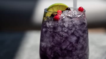 Un vaso de bebida morada con hielo, adornado con una rodaja de lima y bayas rojas, y una pajita.