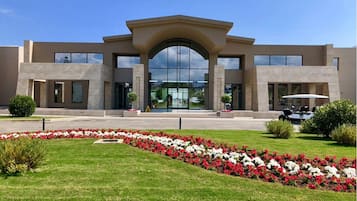 Un edificio moderno con una entrada amplia, un estacionamiento y un jardín bien cuidado con flores rojas y blancas.