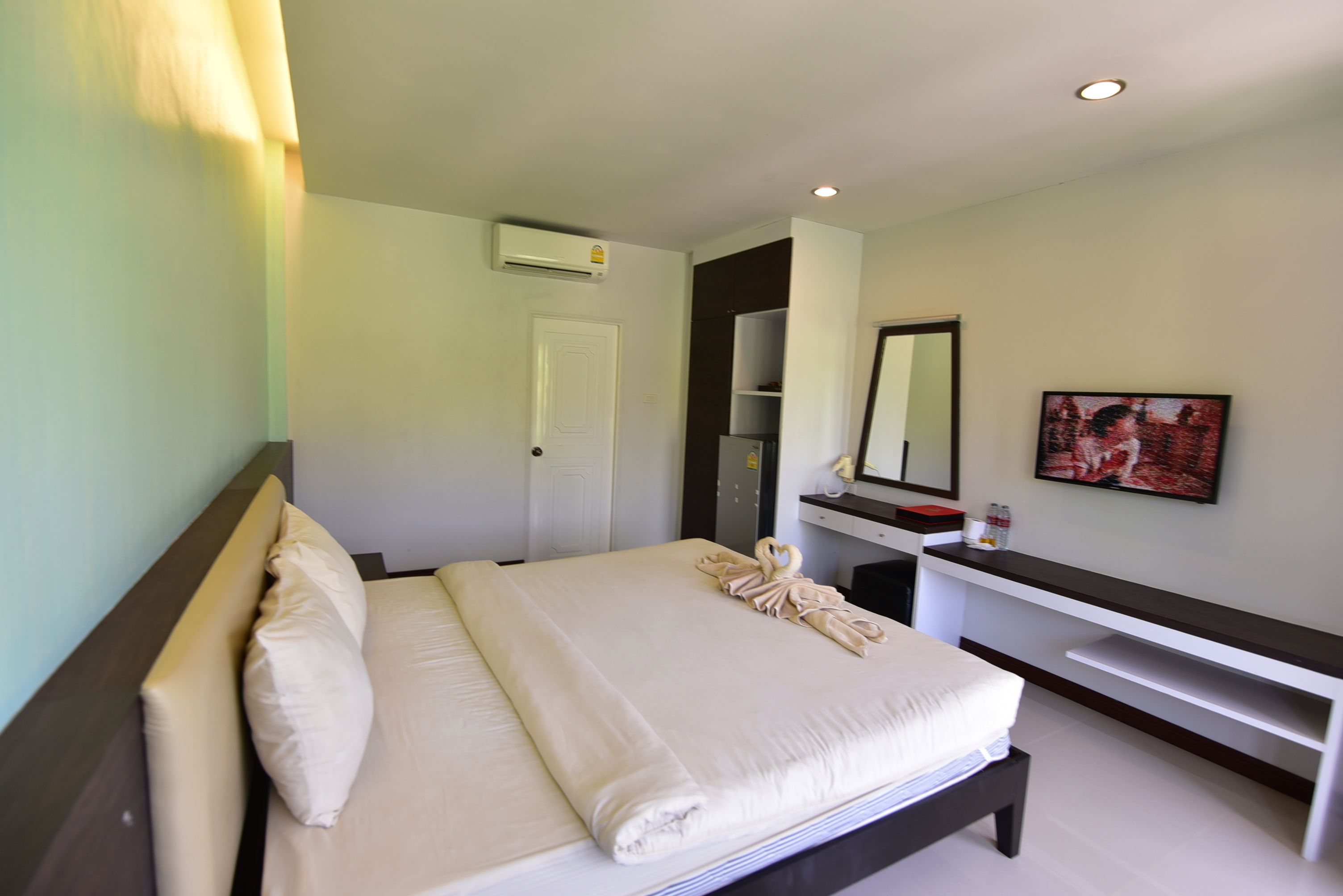 A hotel room with a bed, a desk, a chair, a mirror, and a painting on the wall.