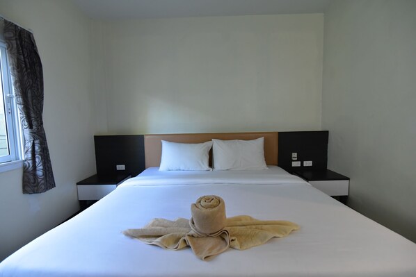 Une chambre d’hôtel avec un lit bien fait, une tête de lit et une fenêtre avec des rideaux.