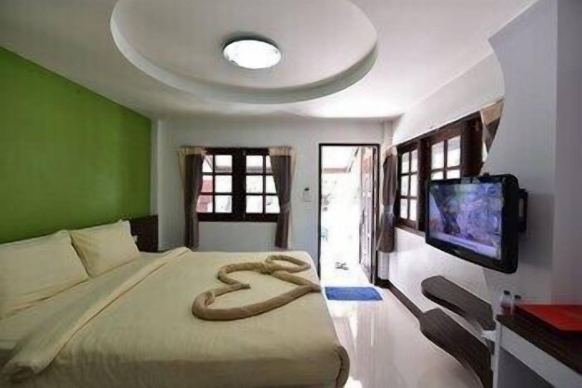 A hotel room with a bed, a television, a window, and a door.
