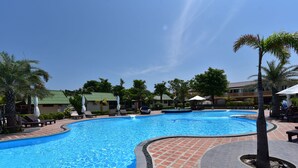 A swimming pool with a curved edge, surrounded by lounge chairs and palm trees.