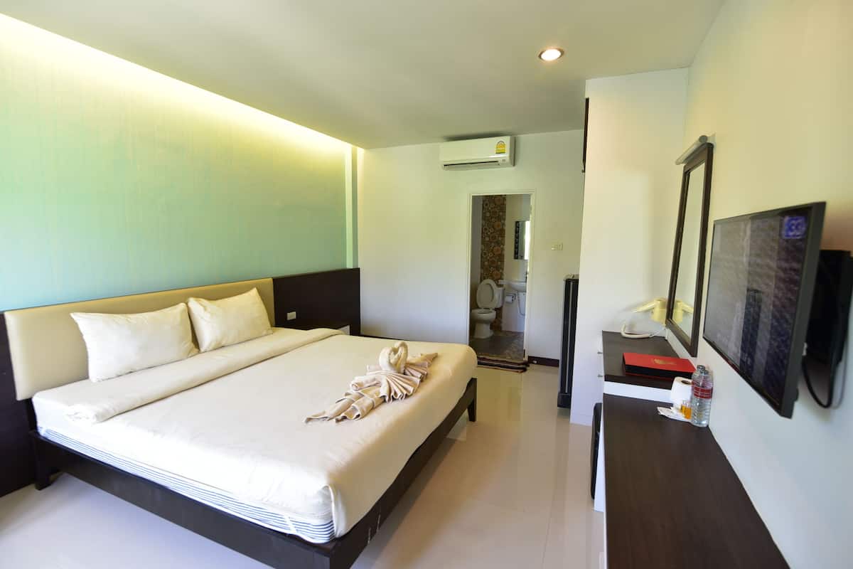 A hotel room with a bed, a desk, a mirror, and a bathroom visible through an open door.