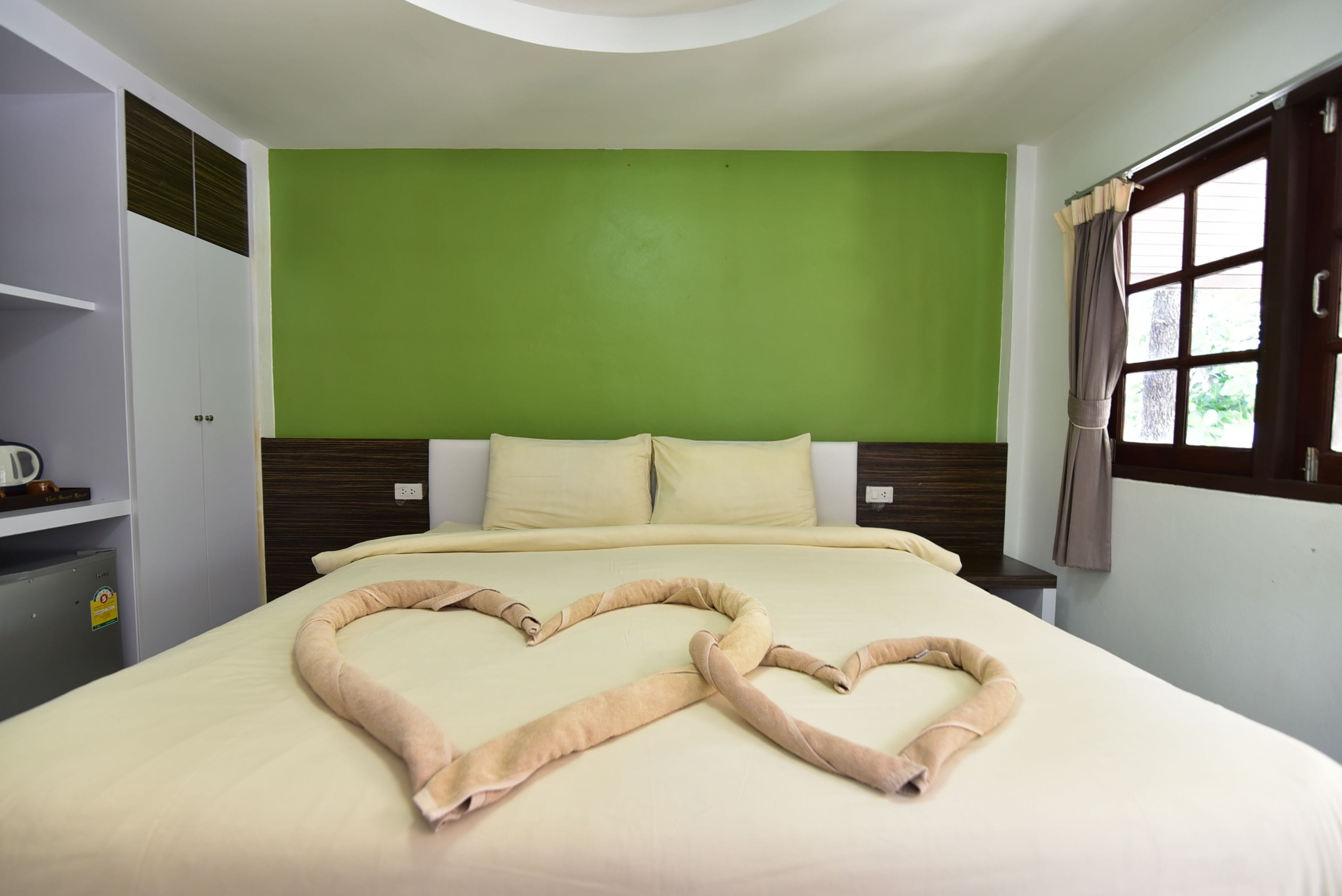 A hotel room with a bed, green walls, a window with curtains, and a wardrobe.