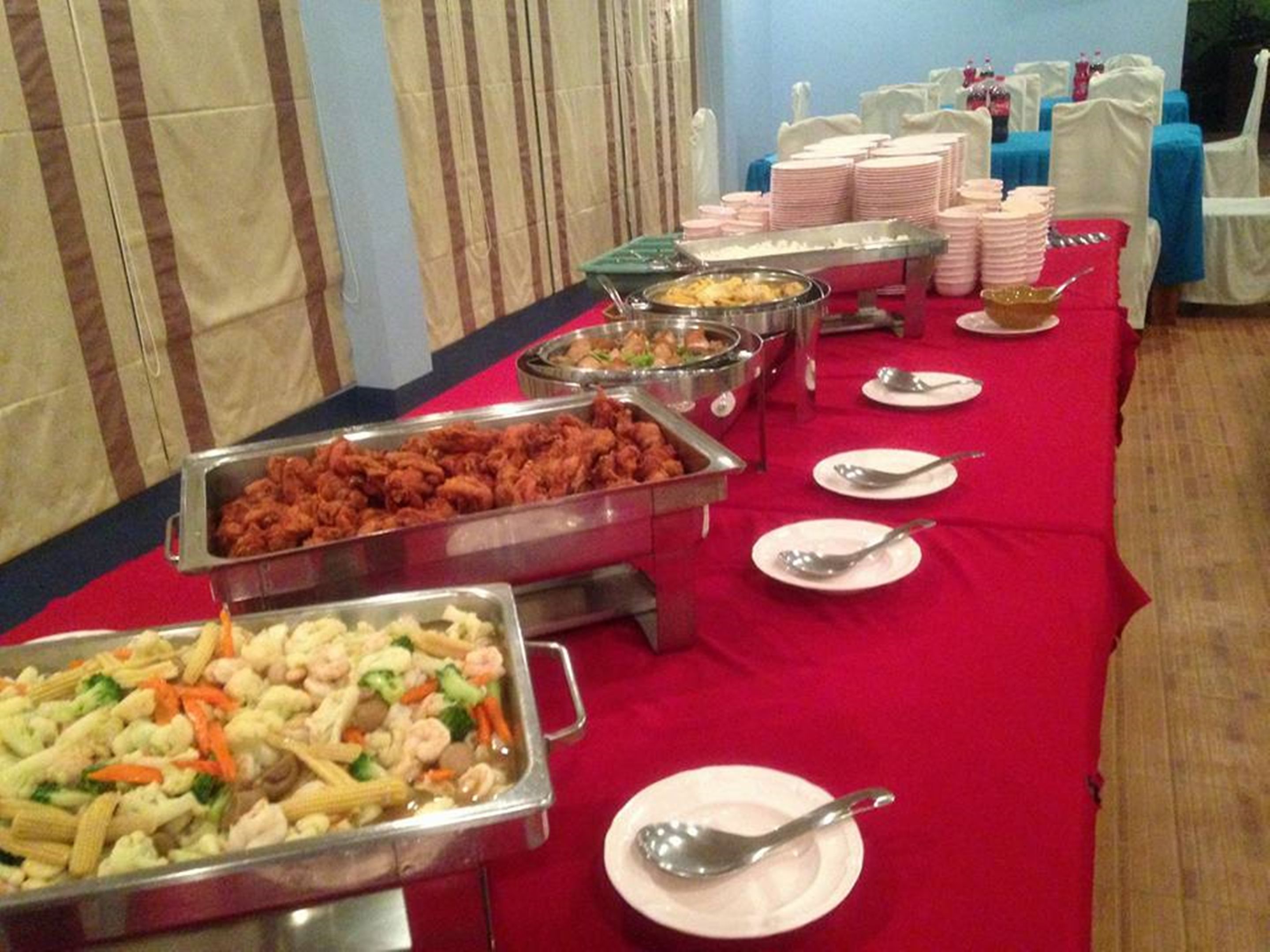 A buffet setup with various food stations, including a tray of fried chicken, a vegetable stir-fry, and several bowls of soup.