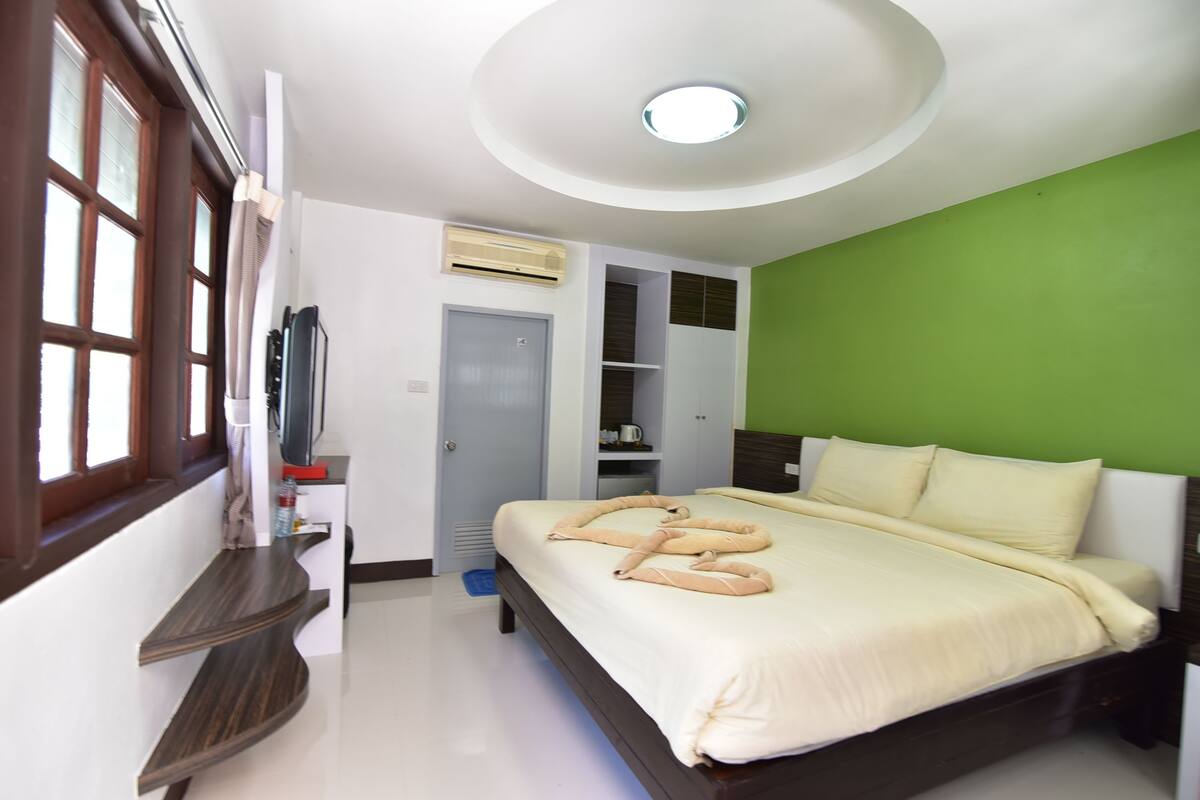 A bedroom with a bed, a television, a wardrobe, and a green wall.