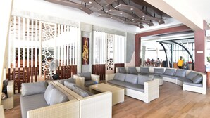 A spacious lounge area with wicker sofas and chairs, a large fan, and a decorative wall with intricate patterns.